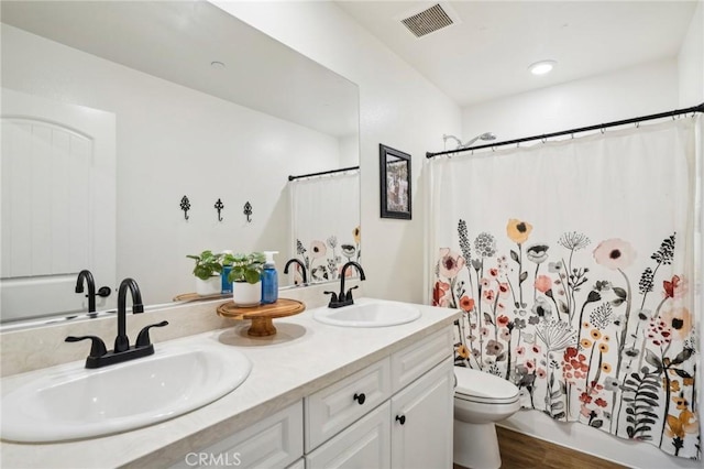 bathroom featuring double vanity, visible vents, toilet, and a sink