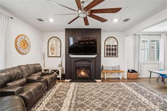 living area featuring a ceiling fan, visible vents, a fireplace, and wood finished floors