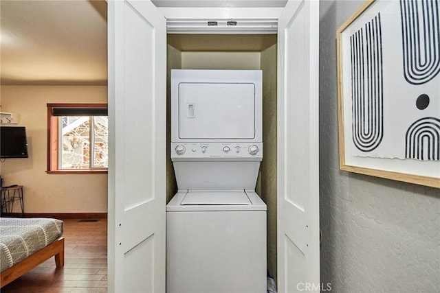 laundry room with baseboards, laundry area, wood finished floors, and stacked washer / drying machine