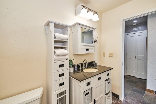 bathroom with stone finish floor, baseboards, vanity, and toilet