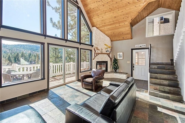 living area with wood ceiling, stone tile flooring, a stone fireplace, and stairs