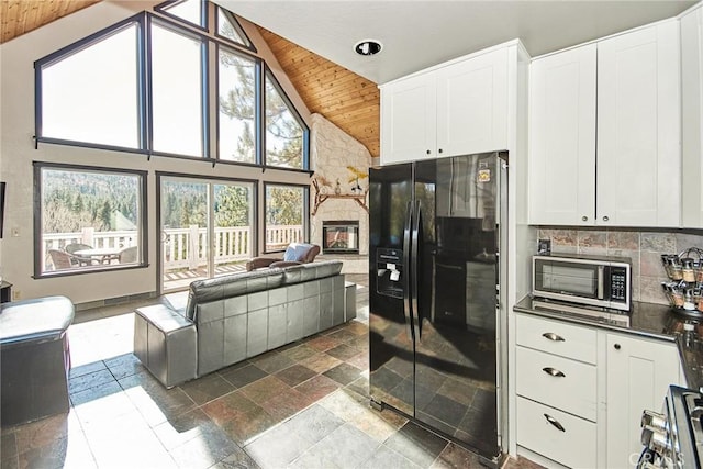 kitchen featuring black fridge with ice dispenser, white cabinets, open floor plan, stainless steel microwave, and dark countertops