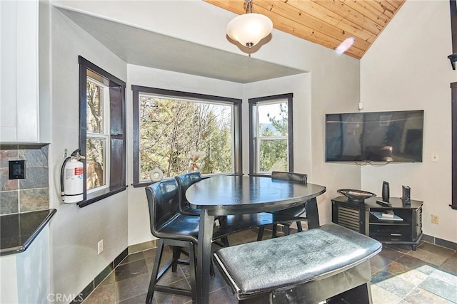 dining room featuring lofted ceiling, wood ceiling, baseboards, and stone tile floors