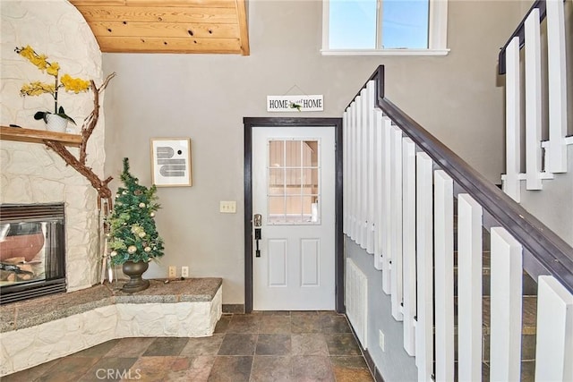 entrance foyer with wood ceiling, stairs, stone finish floor, and a fireplace