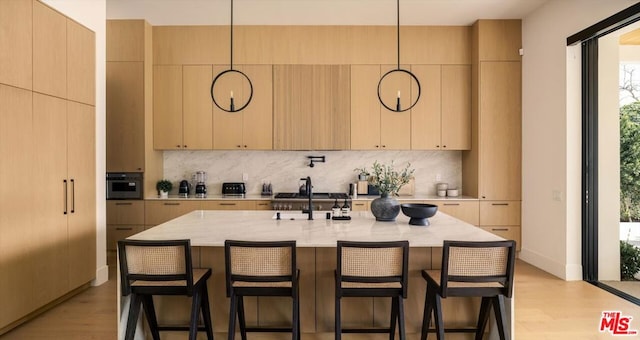 kitchen featuring pendant lighting, an island with sink, light hardwood / wood-style flooring, and light brown cabinets