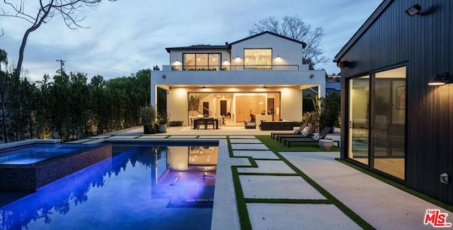 rear view of property with a balcony, an outdoor hangout area, a pool with hot tub, and a patio area