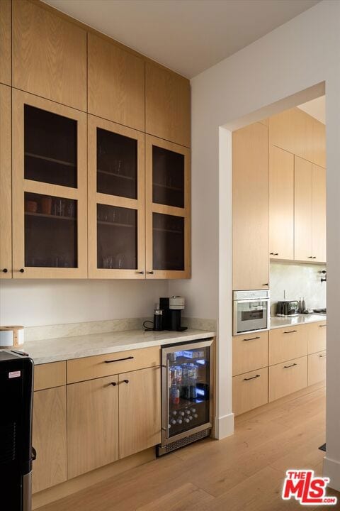 kitchen featuring tasteful backsplash, beverage cooler, stainless steel oven, light brown cabinets, and light hardwood / wood-style flooring