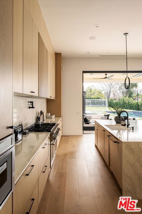 kitchen with hanging light fixtures, light hardwood / wood-style flooring, sink, and high end stainless steel range oven