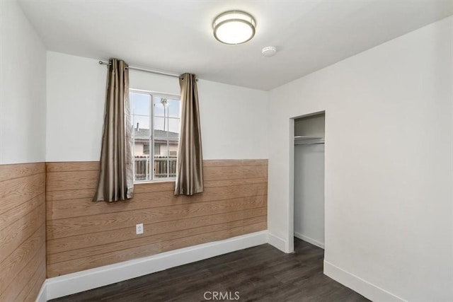 unfurnished bedroom with dark wood-type flooring, wooden walls, and a closet