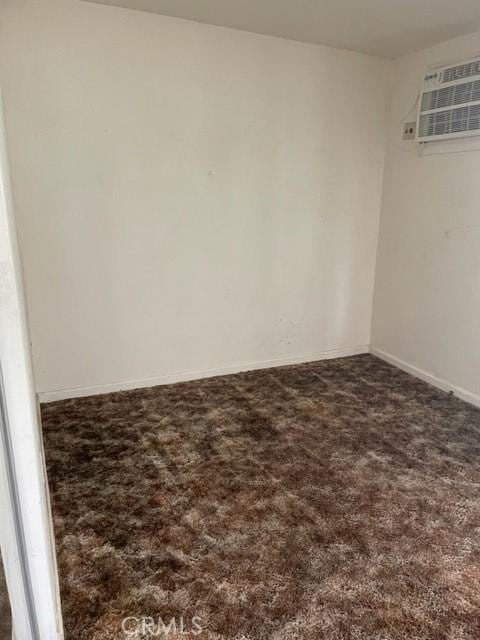 unfurnished room featuring a wall mounted AC, baseboards, and carpet