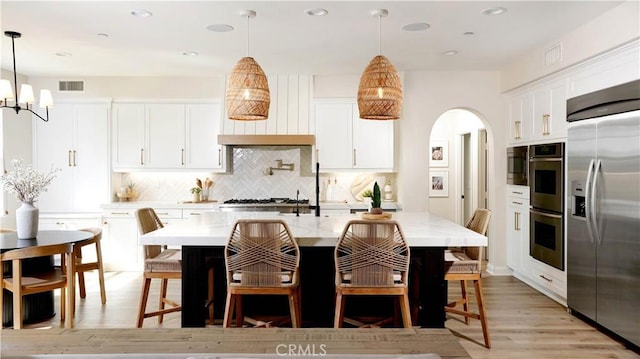 19 Basilica Pl, Ladera Ranch, CA 92694 - kitchen with appliances with stainless steel finishes, arched walkways, light wood-type flooring, backsplash, and a chandelier