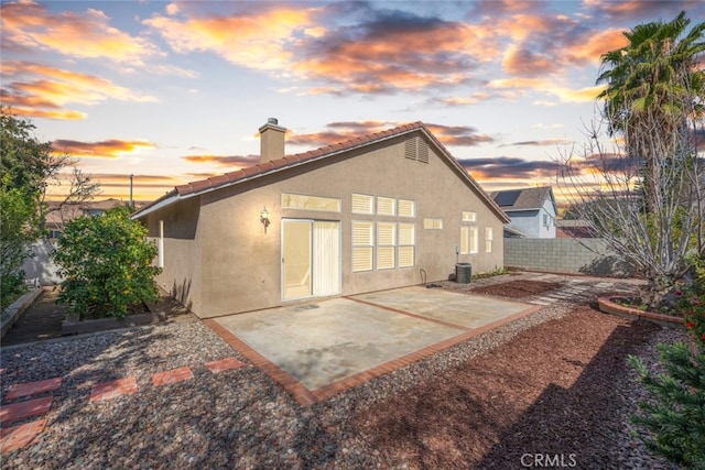 back of property at dusk featuring a patio, a tile roof, a chimney, fence, and stucco siding