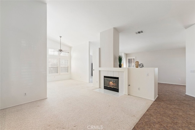 unfurnished living room featuring lofted ceiling, carpet floors, visible vents, a ceiling fan, and a tiled fireplace