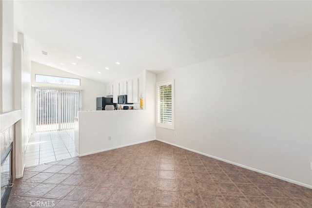 unfurnished living room featuring a healthy amount of sunlight, baseboards, vaulted ceiling, and a tile fireplace