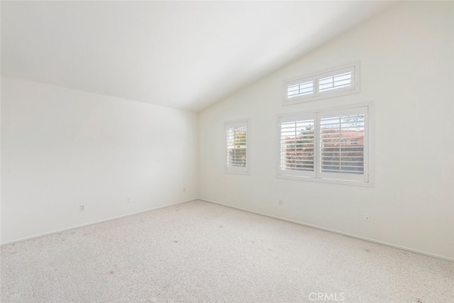 empty room featuring light carpet, vaulted ceiling, and baseboards