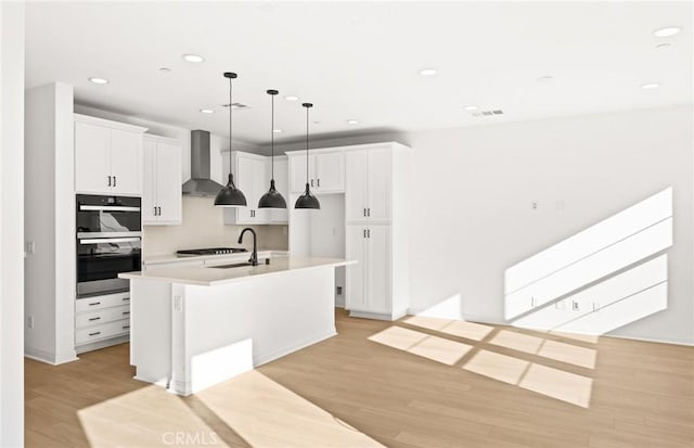 kitchen featuring white cabinetry, sink, a kitchen island with sink, and wall chimney range hood