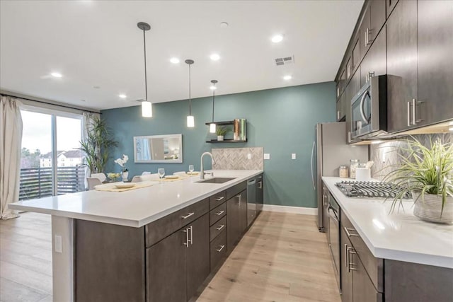 kitchen featuring sink, backsplash, hanging light fixtures, stainless steel appliances, and light wood-type flooring