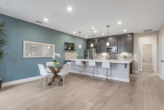 kitchen with a kitchen bar, hanging light fixtures, appliances with stainless steel finishes, an island with sink, and decorative backsplash