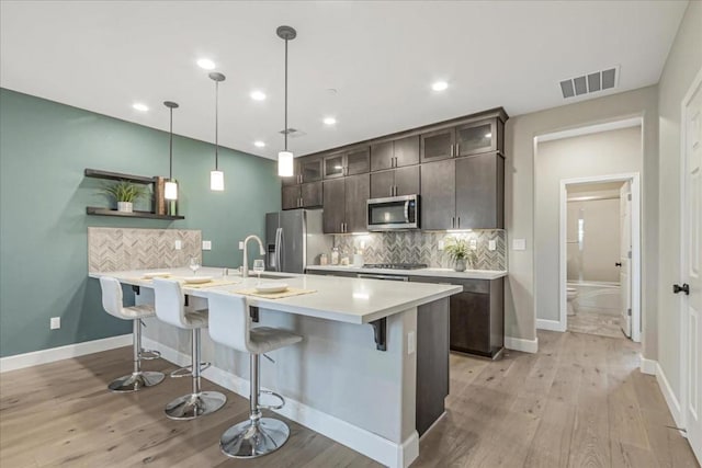 kitchen with dark brown cabinetry, light hardwood / wood-style floors, stainless steel appliances, and a breakfast bar