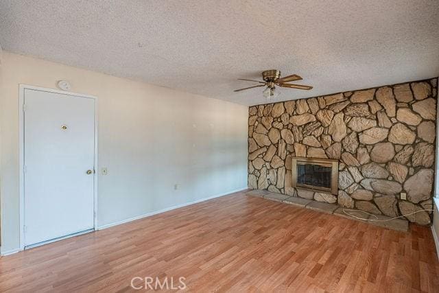 unfurnished living room featuring ceiling fan, a stone fireplace, wood-type flooring, and a textured ceiling