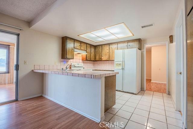 kitchen featuring decorative backsplash, white refrigerator with ice dispenser, tile counters, range, and kitchen peninsula