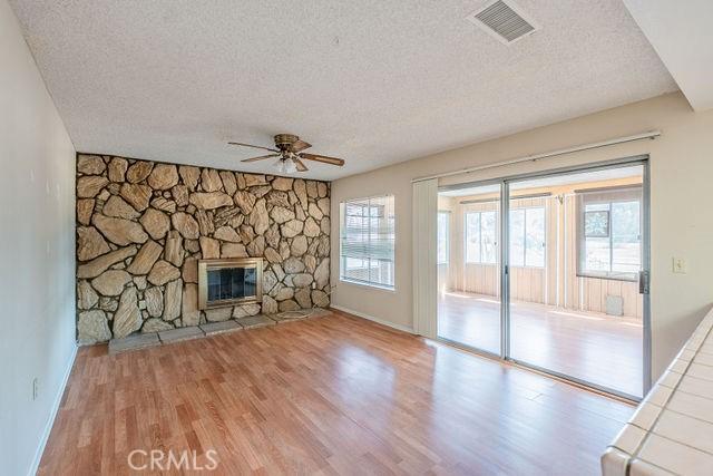 unfurnished living room featuring ceiling fan, a stone fireplace, a textured ceiling, and light wood-type flooring