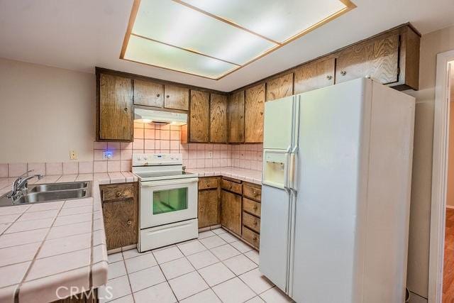 kitchen with sink, white appliances, tile counters, light tile patterned flooring, and decorative backsplash