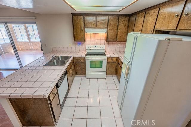 kitchen featuring sink, white appliances, extractor fan, tile counters, and light tile patterned flooring