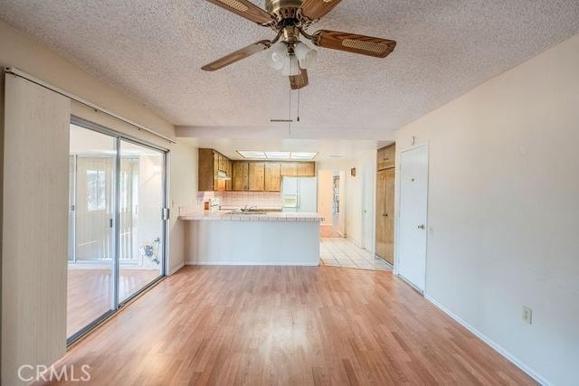 unfurnished living room featuring ceiling fan, a textured ceiling, and light wood-type flooring