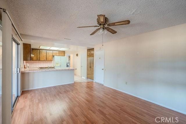 unfurnished living room featuring ceiling fan, light hardwood / wood-style flooring, and a textured ceiling