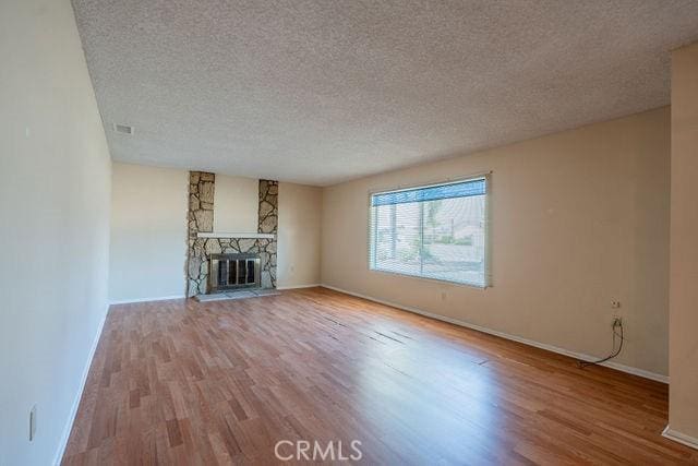 unfurnished living room featuring a stone fireplace, light hardwood / wood-style flooring, and a textured ceiling