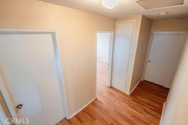 hallway with a textured ceiling and light hardwood / wood-style flooring