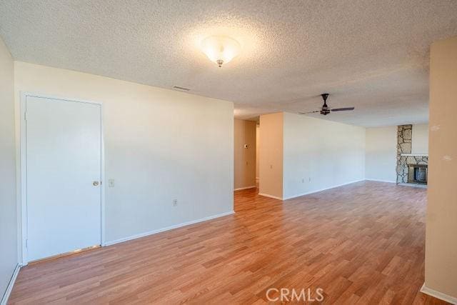 unfurnished room featuring hardwood / wood-style flooring, a fireplace, a textured ceiling, and ceiling fan