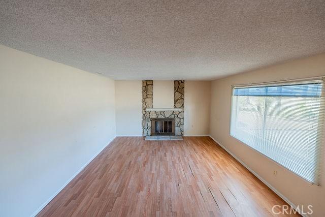 unfurnished living room featuring a stone fireplace, light hardwood / wood-style flooring, and a textured ceiling