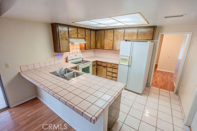 kitchen with tile countertops, sink, decorative backsplash, kitchen peninsula, and white appliances