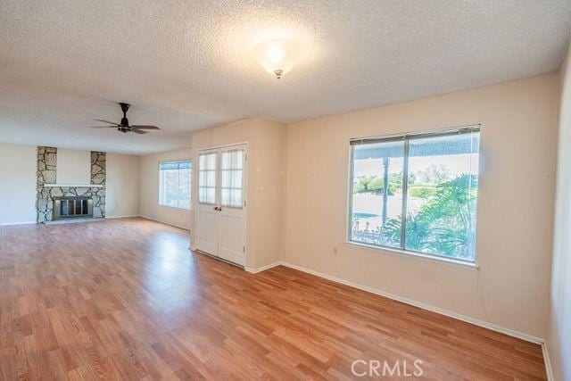 unfurnished living room featuring ceiling fan, a stone fireplace, a textured ceiling, and light wood-type flooring