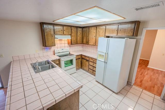 kitchen with light tile patterned flooring, sink, tile counters, kitchen peninsula, and white appliances