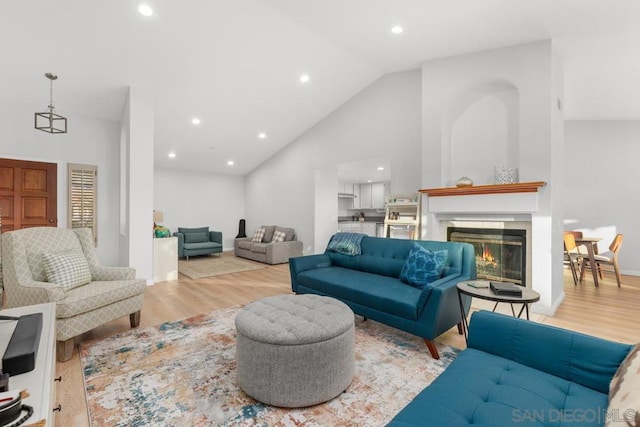 living room featuring high vaulted ceiling, a fireplace, and light hardwood / wood-style floors