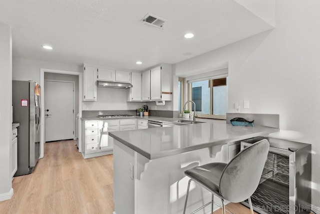 kitchen with a breakfast bar, white cabinetry, light hardwood / wood-style flooring, appliances with stainless steel finishes, and kitchen peninsula