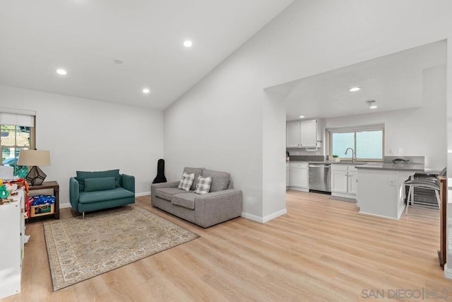 living room featuring high vaulted ceiling, sink, light hardwood / wood-style flooring, and a wealth of natural light