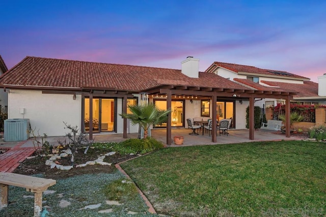 back house at dusk featuring central AC, a pergola, a patio area, and a lawn