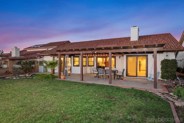 back house at dusk with a patio, a pergola, and a lawn