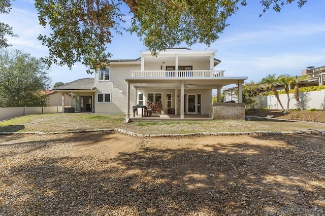 rear view of property with ceiling fan, a balcony, a patio area, and a lawn