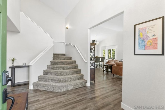 staircase featuring a notable chandelier, hardwood / wood-style flooring, and vaulted ceiling