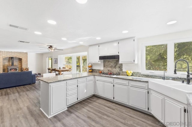 kitchen with white cabinetry, a wood stove, light hardwood / wood-style floors, and kitchen peninsula