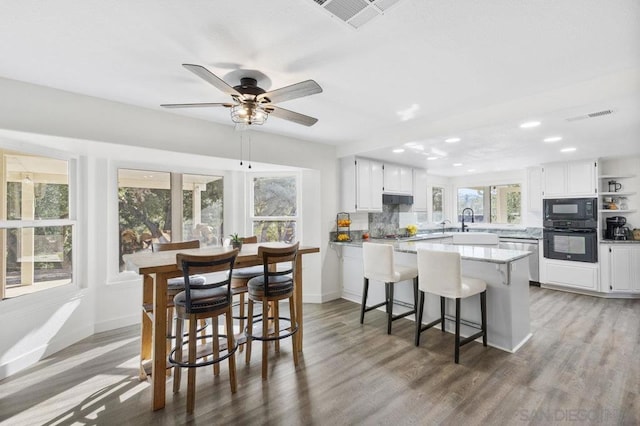 kitchen with white cabinetry, backsplash, a breakfast bar area, and black appliances