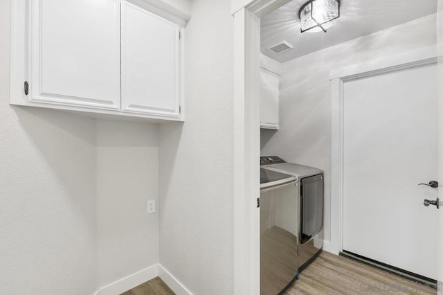 laundry room featuring cabinets, washing machine and dryer, and light hardwood / wood-style flooring