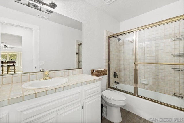 full bathroom with hardwood / wood-style flooring, vanity, toilet, and combined bath / shower with glass door