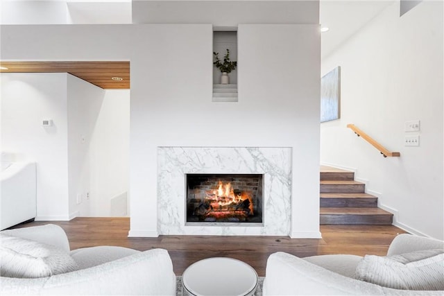 living area featuring a premium fireplace, wood finished floors, visible vents, baseboards, and stairway