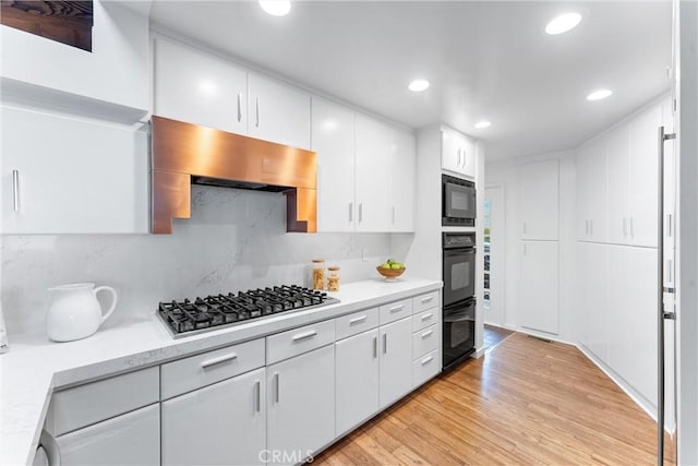 kitchen with light wood finished floors, stainless steel gas stovetop, decorative backsplash, white cabinets, and exhaust hood